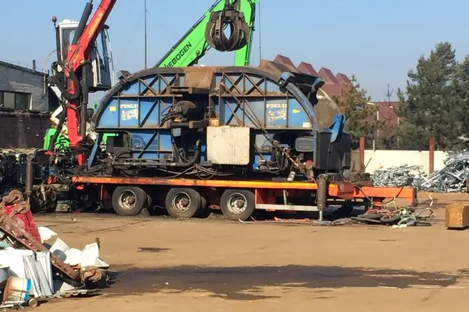 Hydraulická ruka nakladá karosérie starých vozidiel na náves.